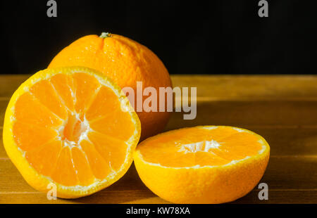 Mandarino maturo frutta sbucciata aperto e posizionare sul vecchio aspetto rustico in legno con gruppo di mandarino frutti al di fuori della messa a fuoco sullo sfondo Foto Stock