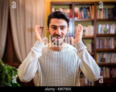Piacevolmente sorpreso bel giovane guardando la telecamera, interni a casa Foto Stock