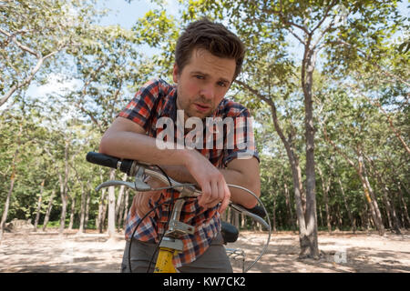 Un giovane uomo è stanco di una bicicletta. Fuori fa caldo e vuole bere. Foto Stock