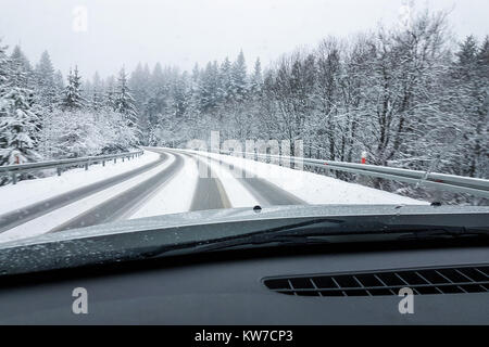 Alla guida di una vettura in cattive condizioni atmosferiche - Una finestra anteriore in prospettiva di una strada innevata durante in inverno in un giorno di nebbia. Foto Stock