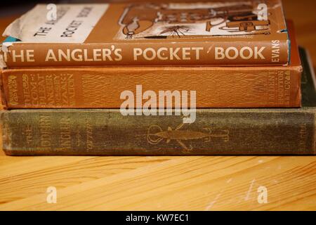 Pila di vecchi libri di pesca su una scrivania in legno, Devon, Regno Unito. L'inverno 2017. Foto Stock