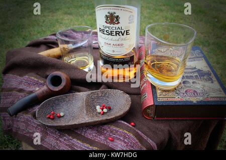 Ancora vita fatta di bottiglie di whisky, due bicchieri, un libro e un tubo di legno e ciotola Foto Stock