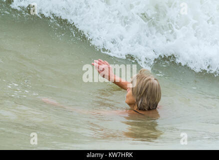 Donna di mezza età il nuoto nel mare senza abbigliamento protettivo con una grande onda si avvicina, in una fredda giornata. Foto Stock