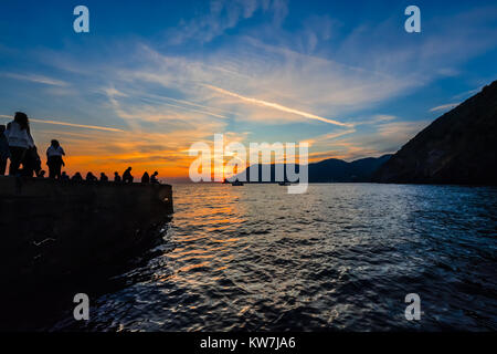 Uno splendido tramonto lungo la costa ligure di Vernazza in Cinque Terre Italia con turisti e barche stagliano contro i colori del mare e del cielo Foto Stock