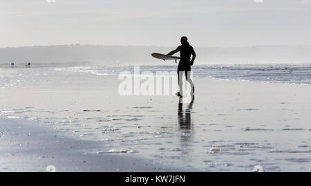 Surfer passeggiate su una spiaggia di sabbia in possesso di una tavola da surf Foto Stock