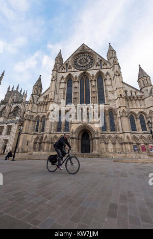 York Centre - sotto il cielo blu, uomo Bicicletta Equitazione attraverso piazza, cicli passato ingresso sud alla magnifica cattedrale di York Minster - North Yorkshire, Inghilterra, Regno Unito. Foto Stock