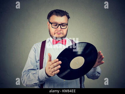 Chunky uomo in abito formale tenendo il vecchio disco di vinile cercando confuso. Foto Stock