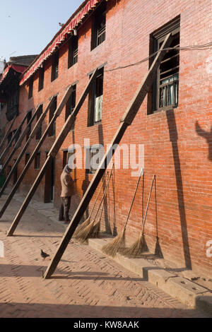 L'uomo sul cellulare sorge accanto al terremoto edificio danneggiato puntellato con supporti in legno a Kathmandu in Nepal Foto Stock