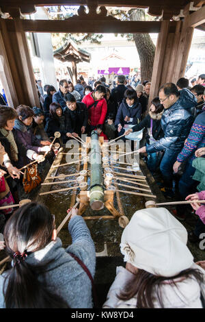 Giappone, Nishinomiya. Primo giorno del nuovo anno. Persone hanno affollato intorno temizuya, bacino di depurazione, utilizzando campionatori a immersione in legno per purificarsi prima di visitare la lucentezza. Molto occupato, gremita di gente. Foto Stock