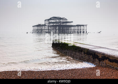La spiaggia di Brighton e i resti del vecchio molo Ovest su un nebbioso giorno in luce piatta, Sussex, Inghilterra, Regno Unito. Foto Stock