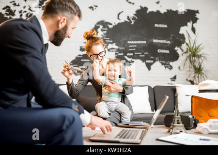 La famiglia felice seduto con uomo agente presso l'agenzia viaggi ufficio con bella mappa sullo sfondo scegliendo un tour per una vacanza estiva Foto Stock