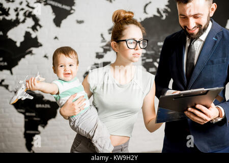 Felice la madre e il bambino, la scelta di tour per una vacanza estiva con agente maschio presso l'agenzia viaggi ufficio con mappa del mondo sullo sfondo Foto Stock