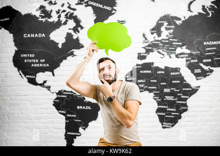 Uomo con una cupola colorata sopra la testa seduto in ufficio con la mappa del mondo sullo sfondo a sognare in viaggio Foto Stock