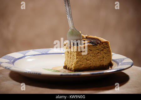 La forcella bloccata nella parte di una cheesecake alla zucca contro sfondo marrone Foto Stock