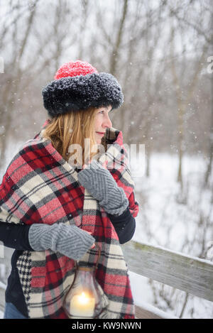 Donna felice fuori a piedi nei boschi mentre la neve è caduta lanterna di contenimento Foto Stock