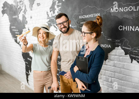 Ritratto di una giovane coppia di viaggiatori scegliendo una striscia di estate in piedi con agente di viaggio sulla mappa del mondo sullo sfondo Foto Stock