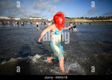 Un nuotatore corre in mare a Barry Island il giorno di Anno Nuovo nuotare a Whitmore Bay, Vale of Glamorgan, South Wales, durante la trentaquattresima edizione annuale di Nuovo Anno Giorno nuotare, che inizialmente avviato quando cinque membri del Jacksons Bay Club bagnino deciso a scrollarsi di dosso i postumi della sbornia con un tuffo, da sommergere completamente se stessi per tre volte. Foto Stock