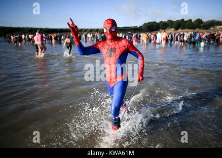 Spiderman corre in mare a Barry Island il giorno di Anno Nuovo nuotare a Whitmore Bay, Vale of Glamorgan, South Wales, durante la trentaquattresima edizione annuale di Nuovo Anno Giorno nuotare, che inizialmente avviato quando cinque membri del Jacksons Bay Club bagnino deciso a scrollarsi di dosso i postumi della sbornia con un tuffo, da sommergere completamente se stessi per tre volte. Foto Stock