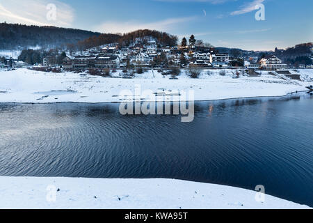 Sera vista sul lago Rursee al villaggio di Rurberg con la neve in inverno in Eifel, Germania. Foto Stock