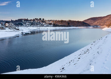 Vista serale oltre il serbatoio lago Rursee al villaggio di Rurberg con la neve in inverno in Eifel, Germania. Foto Stock