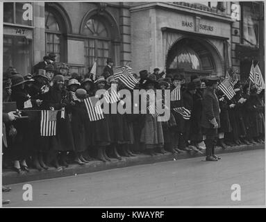 Sorridendo e agitando Stati Uniti bandiere mentre affollato sul marciapiede della strada, curiosi vestito di cappotti e cappelli attendono la sfilata del famoso 369 americano africano di fanteria, precedentemente xv New York i clienti abituali, New York New York, 1917. Immagine cortesia archivi nazionali. Foto Stock