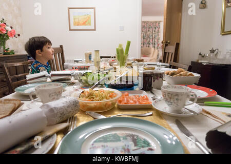Un ragazzo si siede e attende palesemente al tavolo da pranzo per il resto della sua famiglia ad unirsi a lui per mangiare tè di Natale costituito da insalata. Foto Stock