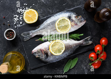 Non cotte fresche dorado o Orate di mare il pesce con le fette di limone e di spezie, erbe e verdure su sfondo di ardesia. Cucina mediterranea. Vista superiore Foto Stock