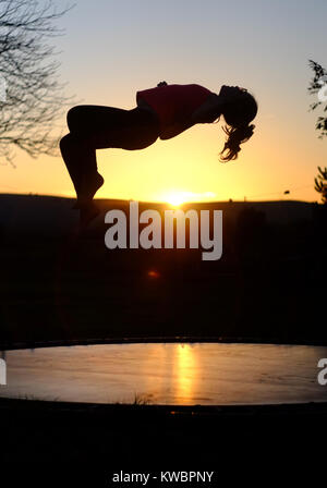 Silhouette di una ragazza su un trampolino al tramonto. Foto Stock
