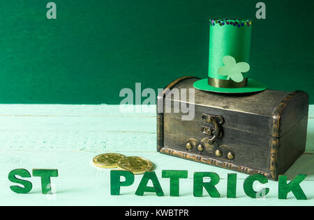 Saint Patrick scritto in verde le lettere in legno, un alto cappello, specifico per St Patrick vacanza, sulla sommità di un vecchio scrigno del tesoro con le monete d'oro nei pressi di esso. Foto Stock