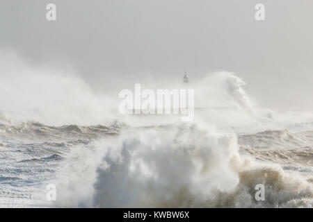 Newhaven, Sussex, Regno Unito; onde si infrangono contro Seawall con faro parzialmente visibile in background Foto Stock