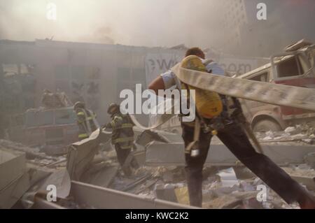 I vigili del fuoco trasporta un tubo attraverso le macerie su settembre 11th, a seguito dell attacco terroristico contro il World Trade Center. La struttura più vicina è un ponte pedonale sul West Side Highway (West St.) che collegava il WTC 1 (Torre nord) con il World Financial Center e Battery Park City. La città di New York, settembre 11, 2001. (BSLOC 2015 2 45) Foto Stock