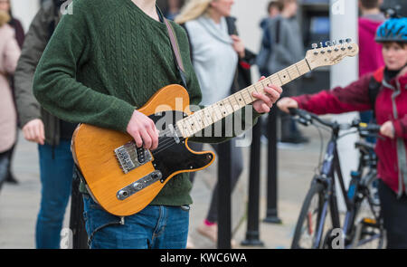 Giovane maschio busker suonando la chitarra in un freddo giorno di inverno nella vivace città di Brighton, East Sussex, Inghilterra, Regno Unito. Foto Stock