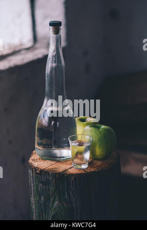 Apple brandy, rustica atmosfera rétro. Bottiglia e unico colpo di vetro con alcool bere e due verde mela frutta. Foto Stock