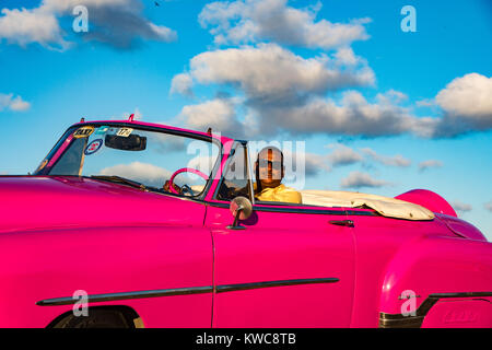 L'Avana, Cuba, 20 Nov 2017 - conducente siede in una rosa Classic American Chevrolet, con Cielo e nubi in background Foto Stock