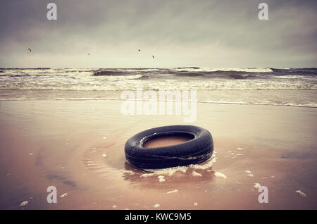 Vecchio pneumatico in gomma nero a sinistra su una spiaggia, ambiente inquinamento concetto, il fuoco selettivo nei toni del colore dell'immagine. Foto Stock