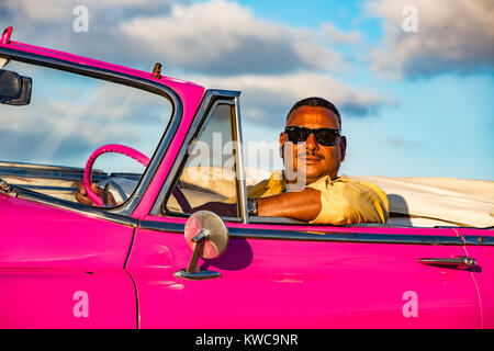 L'Avana, Cuba, 20 Nov 2017 - conducente siede in una rosa Classic American Chevrolet, con Cielo e nubi in background Foto Stock