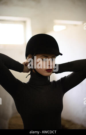 Donna elegante in nero mette il suo cappello sulla prima di un cavallo. Foto Stock