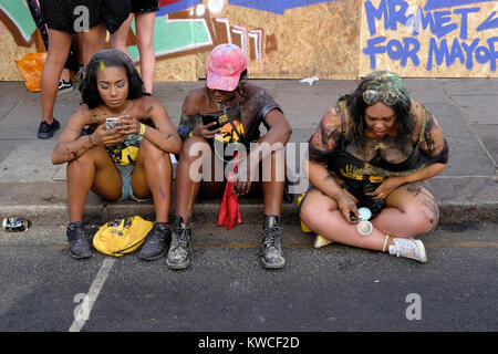 Due giovani donna sfogliare le loro smart phone al carnevale di Notting Hill, London, Regno Unito Foto Stock