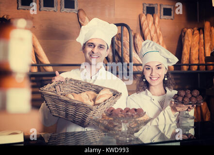 Uomo ospitale e sorridente ragazza offre una deliziosa pasticceria e dolci al cioccolato al forno Foto Stock