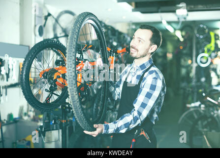 Uomo sorridente master stabilisce una ruota di bicicletta nel suo laboratorio Foto Stock