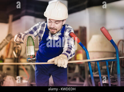 Sorridente uomo di lavoro mettere in pratica le sue abilità con il seghetto alternativo di potenza a un workshop Foto Stock