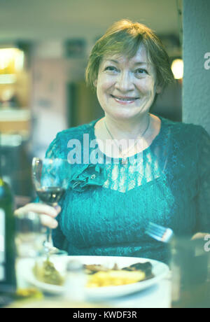 Senior sorridente donna seduta in ristorante e avente bevanda fredda Foto Stock