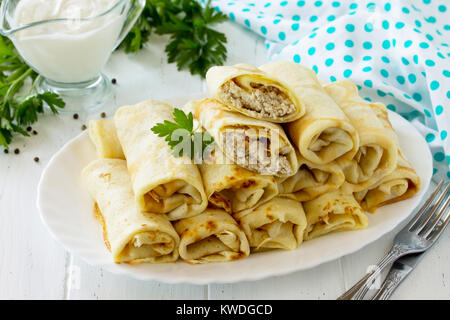 Frittelle. Frittelle con ripieno di carne, servito con panna acida in salsa di cucina tavolo in legno. Foto Stock