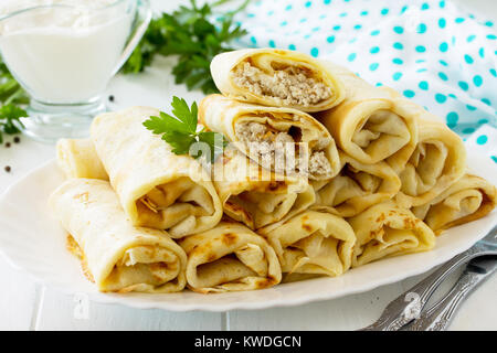 Frittelle. Frittelle con ripieno di carne, servito con panna acida in salsa di cucina tavolo in legno. Foto Stock