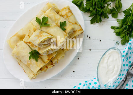 Frittelle. Frittelle con ripieno di carne, servito con panna acida in salsa di cucina tavolo in legno. Lay piatto. Vista da sopra con copia spazio. Foto Stock