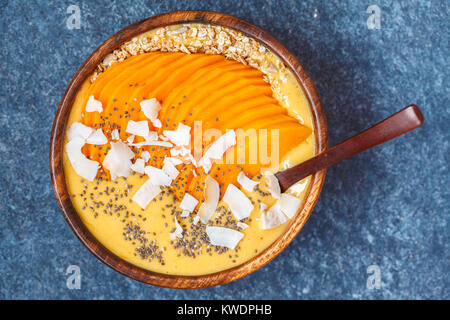 Una sana colazione frullato di mango ciotola con semi di Chia, fette di mango, fette di noce di cocco e le OAT granola. Sano cibo vegan concetto. Foto Stock