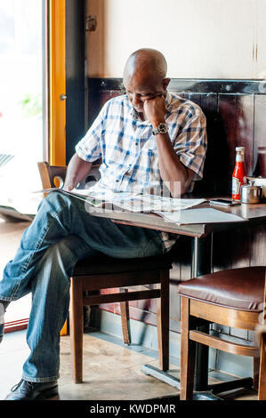 Manb leggendo il giornale in coffee shop, Kampala, Uganda Foto Stock