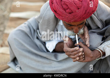 Di scena a Pushkar Camel Fair, uomo in turbante rosso accendere una sigaretta, Pushkar, Ajmer, Rajasthan, India Foto Stock