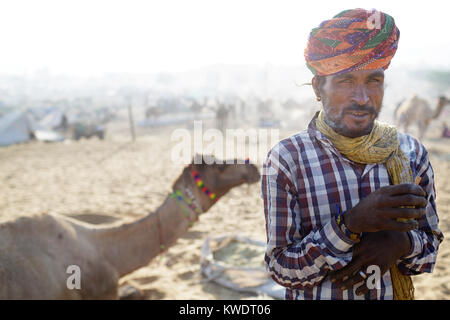 Di scena a Pushkar Camel Fair, ritratto di un operatore che indossa un turbante colorato con un cammello nel retro, Pushkar, Rajasthan, India Foto Stock