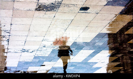 La riflessione ombra silhouette di un uomo sotto l'ombrello rosso a piedi nella città vecchia piazza modellato sotto la pioggia Foto Stock